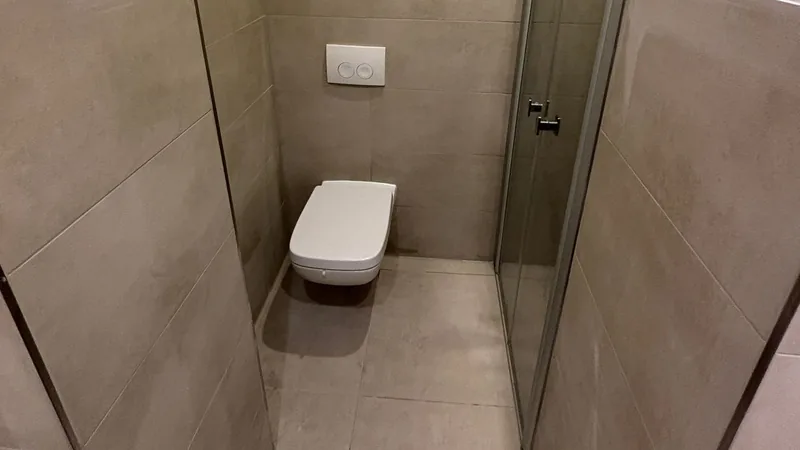 Schmales Gäste-WC mit Wand-WC, Glastür und großformatigen grauen Fliesen