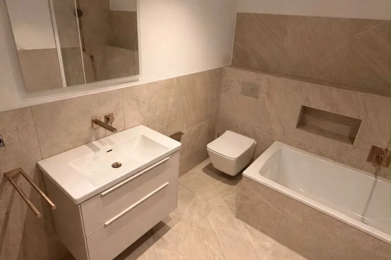 Badfliesen: Bad mit großformatigen Fliesen in heller Steinoptik, Waschtisch mit Unterschrank, Wand-WC und Badewanne