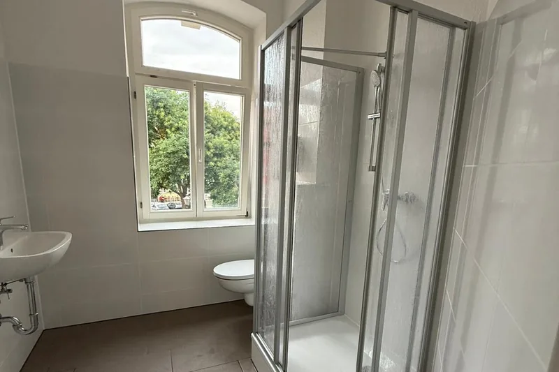 Bad günstig sanieren: Saniertes Altbaubad mit Bogenfenster, Duschkabine, kleinem Waschbecken und Wand-WC